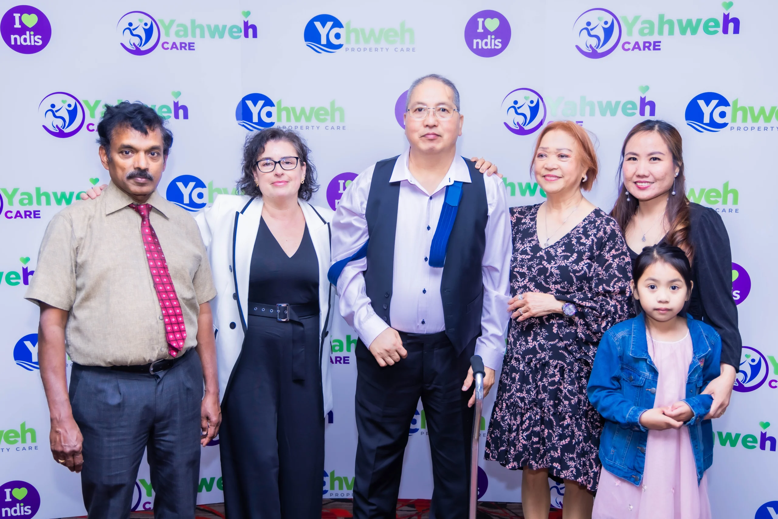 Group photo of five individuals standing in front of a blue Yahweh Care backdrop 